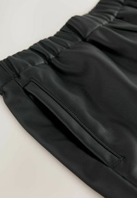 Schwarze Kunstlederhose mit glatter Textur, elastischem Bund und seitlichen Taschen mit ordentlich genähten Nähten.