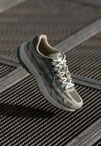 Buty sportowe z siateczkową cholewką w kolorze zielonym i beżowym, z teksturowaną podeszwą, lekkimi sznurowadłami i subtelnym akcentem logo.