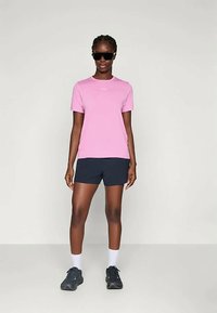 Roosa lühikeste varrukatega t-särk ümarate kaelustega, kombineeritud tumesiniste lühikeste pükstega. Mudel kannab musti päikeseprille ja tumedaid spordijalatooteid.