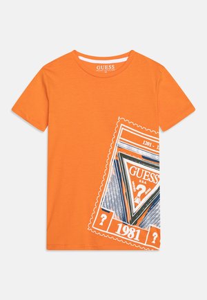 Orangenes Baumwoll-T-Shirt mit großem weißem und marineblauem Stempel-Design mit dem Schriftzug "GUESS" und der Zahl "1981". Gerundeter Rundhalsausschnitt.