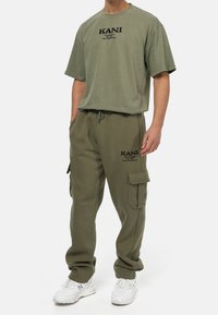 Olijfgroene katoenen t-shirt met zwart logo en bijpassende cargobroek met zijzakken en een elastische tailleband, gecombineerd met witte sneakers.