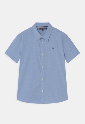 Kortærmet skjorte med knapper i lysblå bomuld, med spids krave og et lille logo på brystet. Har en lige kant og knapper.