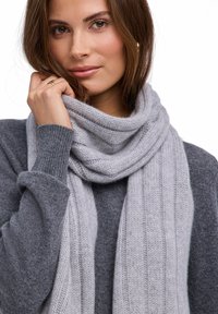 Jasnoszary dziergany szalik owinięty wokół szyi, z teksturowanym wzorem prążkowanym. Widoczny jest miękki, ciepły materiał z mieszanki wełny.