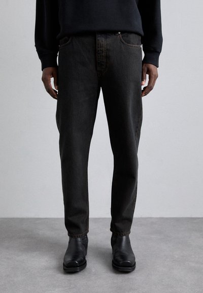 Pantaloni in denim nero con taglio dritto, caratterizzati da cuciture a contrasto e tasche frontali, abbinati a stivaletti neri. Texture opaca.