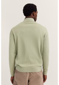 Pullover verde chiaro, realizzato in materiale morbido, con colletto alto e polsini e orlo a costina. Texture liscia, design semplice.