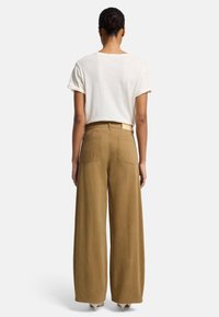 Pantaloni khaki a gamba larga in cotone, con vita alta e due tasche posteriori, abbinati a una semplice t-shirt bianca con maniche arrotolate.