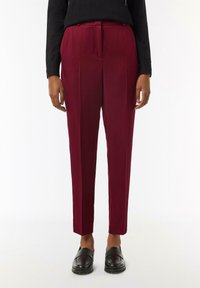 Bordowe spodnie o dopasowanym kroju, z dwoma fałdami z przodu, o gładkiej fakturze i skróconej długości, w połączeniu z czarnymi mokasynami.