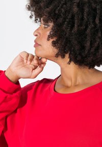 Rotes Sweatshirt mit Rundhalsausschnitt und langen Ärmeln, aus strukturiertem Stoff. Seitenansicht einer Person, die das Kinn auf die Hand stützt.