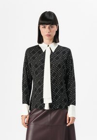 Black patterned blouse with a white collar and tie, featuring a diamond design and solid white cuffs, paired with a burgundy leather skirt.