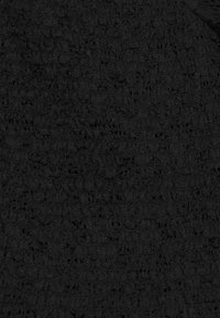 Svart texturerad tyg som har ett subtilt mönster med varierande densiteter och upphöjda element, vilket skapar en lager-på-lager visuell effekt.