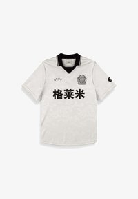 Jersey blanco de manga corta con cuello negro. Presenta una sutil textura floral y texto impreso en negro. Logo en el pecho y la manga.