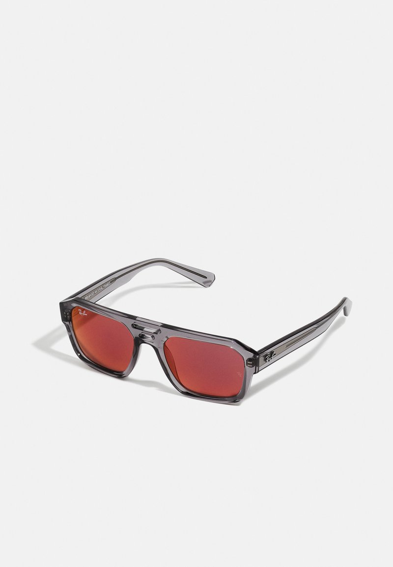 Occhiali da sole con una montatura in plastica grigia e lenti rosse, caratterizzati da una forma ottagonale e un discreto logo Ray-Ban sulle tempie.