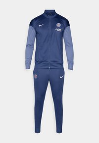 Nike treningsdress med en marineblå jakke med glidelås foran og logo, supplert med matchende smale bukser. Glatt stoff med kontrasterende ermer.
