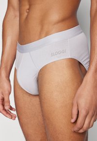 Weiße SLOGGI-Herrenslip mit weichem Bund, glattem Stoff und minimalistischem Design, mit einem dezenten Logo am Bund.