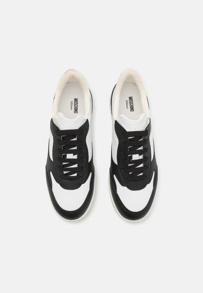 Black and white sneakers featuring a smooth texture, rounded shape, prominent lacing, and branding on the tongue and insole.