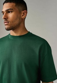 Camiseta de algodón verde con cuello redondo, mangas cortas y un acabado texturizado y suave. Presenta detalles en las costuras de los hombros para mayor estilo.