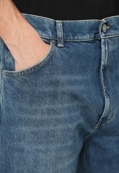 Jeans in denim azzurro chiaro con una tasca visibile e un bottone in metallo. Il tessuto presenta una sottile texture e dettagli di scolorimento lungo i bordi.