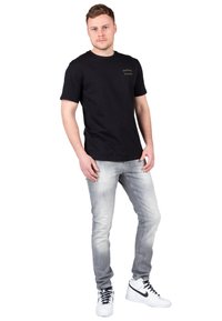 Sort bomulds T-shirt med rund halsudskæring og korte ærmer, parret med lysegrå jeans og hvide sneakers med sorte accenter.