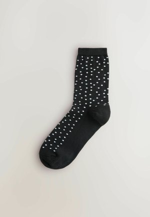 Sort sok med hvide polkaprikker, mellemlang, lavet af et blødt stof, med ribbet kant og glat tekstur.