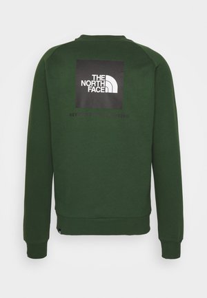 Ciemnozielona bluza z długim rękawem, z logo The North Face w białym kolorze na czarnej kwadratowej naszywce umieszczonej na środku górnej części pleców.