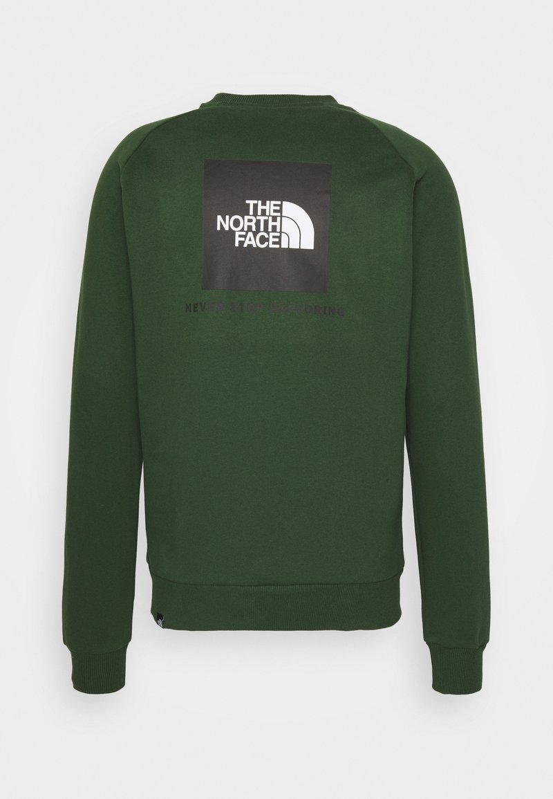 Sweat-shirt à manches longues vert foncé avec le logo The North Face en blanc sur un patch carré noir centré dans le haut du dos.