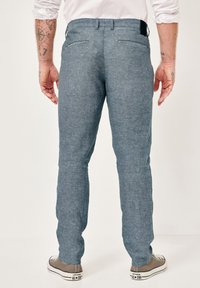 Light blue, textured trousers with a straight fit, featuring two back pockets, paired with gray sneakers. Simple, casual design.