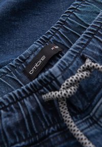 Shorts de mezclilla con cintura elástica, que presentan una etiqueta negra con el texto "ombre" y un cordón en un patrón de cuadros. Color azul oscuro.