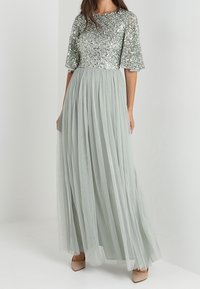 Lång, ljusgrön klänning med en paljetterad överdel och svalande ärmar. Flödande tullekjol som sträcker sig till golvet. Enkla beige klackar kompletterar outfiten.