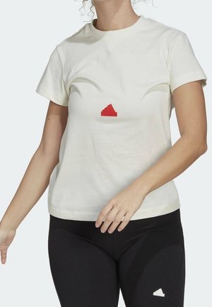 Frau trägt ein weißes kurzärmeliges T-Shirt mit rotem Adidas-Logo und schwarze Leggings mit kleinem weißem Sneaker-Logo.