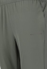 Grå träningsbyxor i lättviktig tyg, med elastisk midja och en subtil logotyp tryckt på låret. Slät textur.