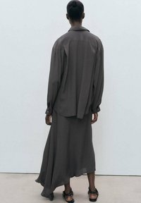Conjunto de camisa y falda de color gris oscuro, largo y fluido, hecho de una tela liviana, con un corte holgado y un dobladillo asimétrico. Sandalias planas completan el look.