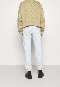 Brun sweatshirt med cirkulära svarta mönster, tillsammans med ljusblå sweatpants med liknande små tryck, bärs med svarta ankelstövlar.