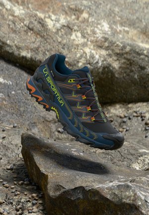 Black and blue trail running shoe with textured mesh upper, vibrant accents, and rugged sole. Notable for its lightweight design and grip.