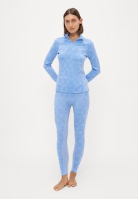 Ανοιχτό μπλε θερμική μπλούζα με μακρύ μανίκι και αντίστοιχες κολάν που διαθέτουν σχέδιο νιφάδας χιονιού. Μαλακό υλικό με κολάρο με φερμουάρ και εφαρμοστή γραμμή.