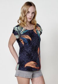 Haut à manches courtes à fleurs bleu marine foncé avec des feuilles tropicales vibrantes en vert et orange. Tissu léger avec une coupe décontractée.