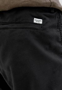 Black cotton pants featuring a back pocket with a white "JACK & JONES" label sewn on. Smooth texture with a classic design.