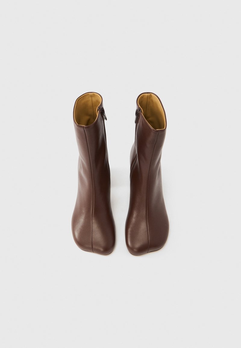 Brown leather ankle boots with a smooth texture, side zippers, and a rounded toe design. Interior lined in contrasting yellow.