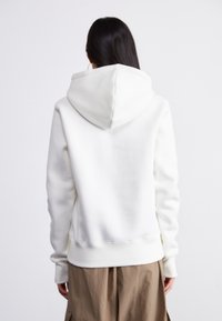 Haut de hoodie en polaire blanche avec une capuche tridimensionnelle, des bords-côtes au niveau des poignets et une coupe décontractée, présentant une texture lisse et un design uni.
