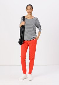 Stripet svart og hvit langermet topp, røde bukser og hvite joggesko. Modellen poserer med en stor svart totebag. Enkelt, uformelt antrekk.