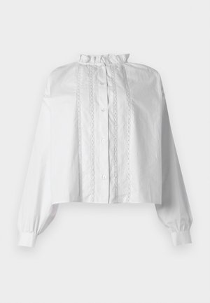 Λευκό κοντό μπλουζάκι με μακριά φουσκωτά μανίκια, γιακά με βολάν, κουμπιά μπροστά και κάθετες λεπτομέρειες με δαντέλα.