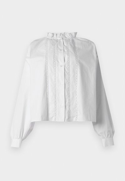 Λευκό κοντό μπλουζάκι με μακριά φουσκωτά μανίκια, γιακά με βολάν, κουμπιά μπροστά και κάθετες λεπτομέρειες με δαντέλα.