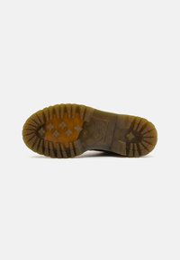 Suela de zapato de goma con ranuras profundas, que presenta una superficie texturizada y un color marrón translúcido. Ofrece agarre y durabilidad.