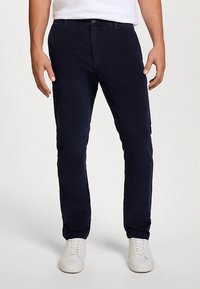 Pantalon en velours côtelé bleu marine à coupe slim, avec poches avant, passants de ceinture et texture douce. Associé à des baskets blanches.