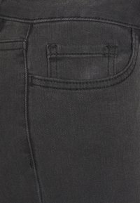 Detalhe do bolso de jeans de ganga pretos com costura, um design clássico de bolso traseiro e um tecido suave.