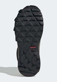 Čierna gumová podrážka s hlbokými trakčnými výstupkami, výstižne zobrazuje značku "adidas TRAXION" v červenej farbe, navrhnutá pre grip na rôznych terénoch.