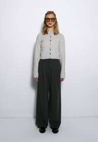 Jasnoszary wełniany kardigan z czarnymi guzikami zestawiony z ciemnymi spodniami o wysokim stanie i szerokich nogawkach oraz czarnymi butami na platformie.