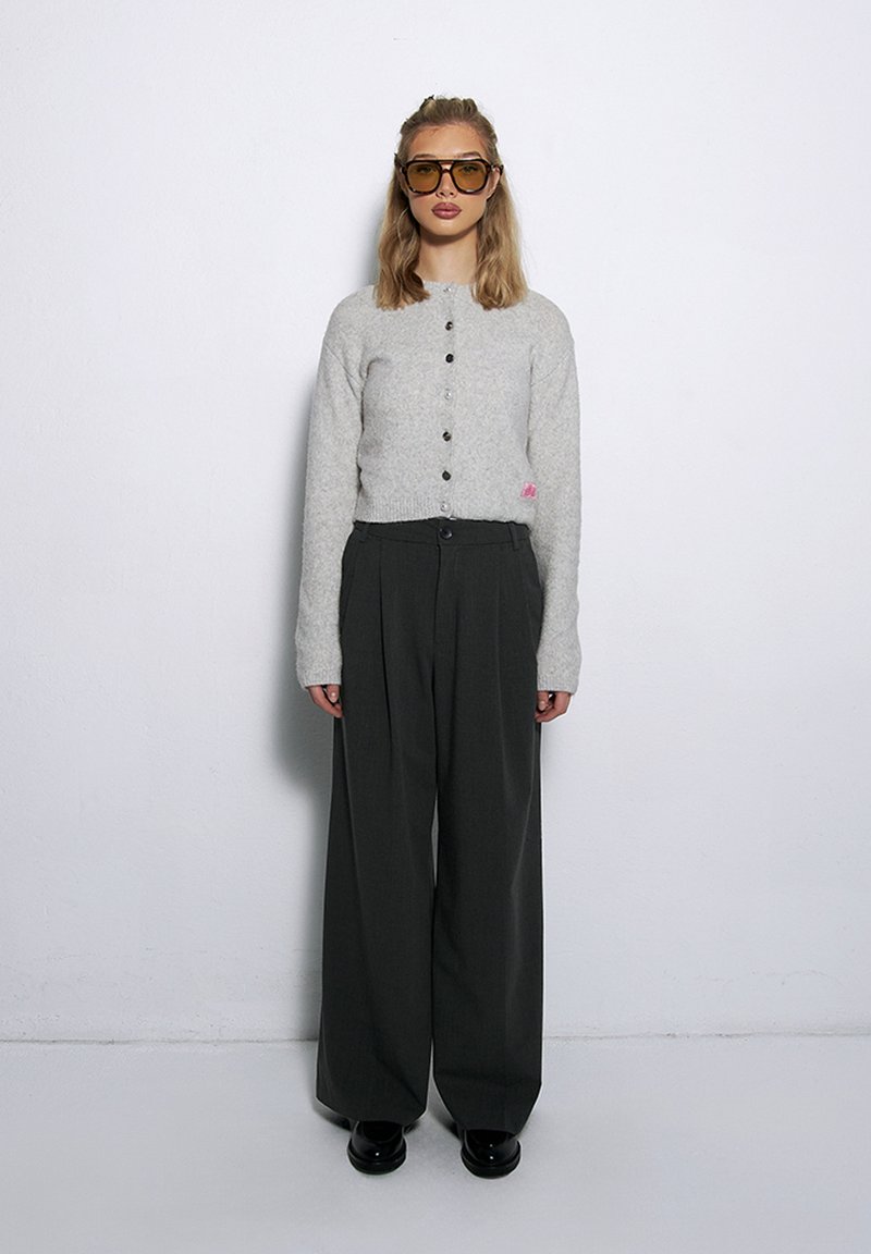 Jasnoszary wełniany kardigan z czarnymi guzikami zestawiony z ciemnymi spodniami o wysokim stanie i szerokich nogawkach oraz czarnymi butami na platformie.