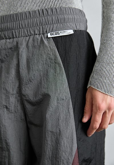 Pantalons de survêtement GCDS avec une taille élastique, présentant une superposition texturée dans des nuances de gris et de noir, et une étiquette logo sur la taille.