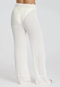Pantaloni bianchi a gamba larga con vita arricciata. Il tessuto testurizzato presenta strisce oro verticali, un design fluido e un orlo leggermente svasato.