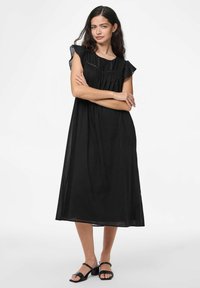 Juoda, iki kelių ilgio suknelė su plačiomis rankovėmis, suburta liemeniui ir dekoratyviniu siuvinėjimu. Audinys atrodo lengvas ir pralaidus orui.